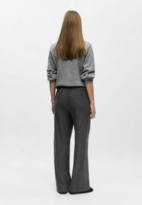 Grå sweater med opmærksomhed på manchetterne og løs pasform, parret med mørkegrå brede bukser. Glat tekstur, ingen synlige mønstre eller hardwaredetaljer.