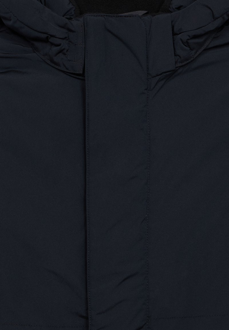 Marineblaue Pufferjacke mit hochgeschlossenem Kragen, ausgestattet mit einem Frontreißverschluss und einer glatten, matten Stofftextur. Minimalistisches Design, keine sichtbaren Muster.