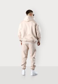 Hellbeige Sweatshirt und passende Jogginghose aus weichem Stoff, mit elastischen Bündchen, lockerer Passform und weißen Sneakern.