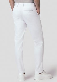 Białe bawełniane spodnie o dopasowanym kroju, z tylnymi kieszeniami i gładką fakturą, w połączeniu z białymi trampkami.