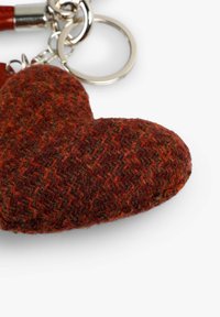 Llave en forma de corazón hecha de tela texturizada con un patrón de espiga en rojo y marrón, con un llavero y cadena de metal plateado.