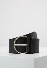Ceinture en cuir noir avec une large sangle et une boucle circulaire en argent, présentant une texture lisse et un design minimaliste.