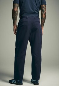 Donkerblauwe broek van soepel materiaal, met twee achterzakken. Gecombineerd met donkerblauwe schoenen met lichtblauwe strepen.