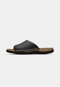 Sandale à glissière en cuir noir avec un coussin tan, couture décorative beige et semelle en caoutchouc noire, montrée en profil latéral.