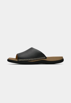 Black leather slide sandal with tan cushioned footbed, decorative beige cross-stitching, and black rubber sole, shown in side profile.