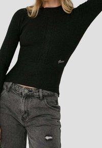Schwarzer gerippter Pullover mit hohem Kragen und Zopfmuster. Kombiniert mit ausgewaschenen grauen Denim-Jeans mit fransiger Tasche.