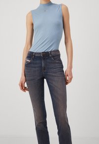 Ljusblå ärmlös topp i ribbat tyg, kombinerad med mörkblå jeans med en lätt slitning vid knäet.