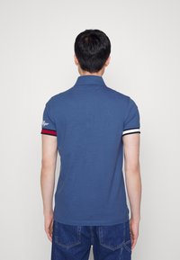 Mörkblå pikétröja med mjuk textur, featuring korta ärmar med röda och vita ränder, och en klassisk krage.