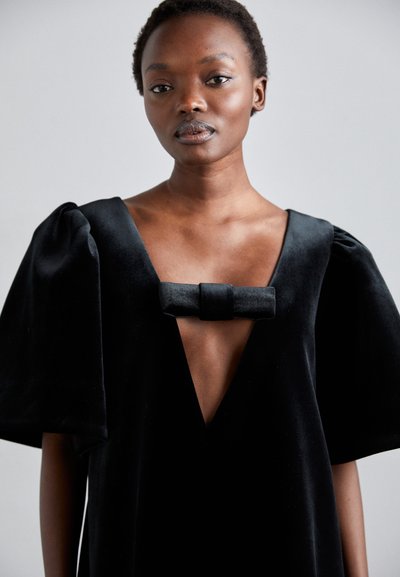 Black velvet dress with a deep v-neck, oversized puff sleeves, and a bow detail at the chest. Smooth texture and elegant silhouette.