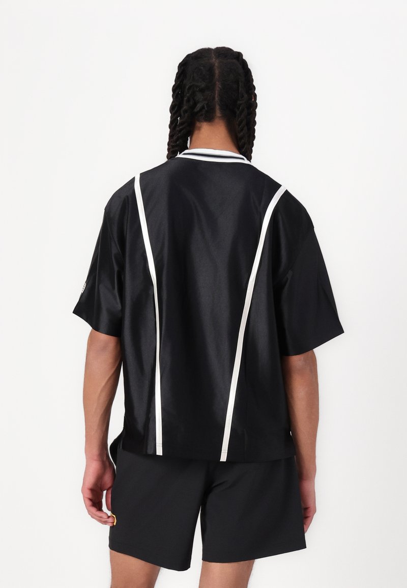 Chemise noire à manches courtes avec rayures blanches sur les côtés et détail de col, présentant une texture lisse et une coupe décontractée, associée à un short noir.
