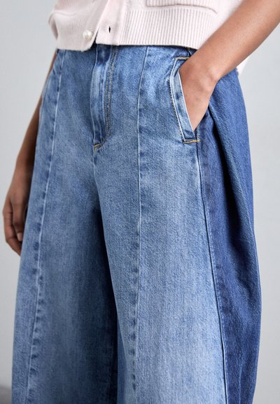 Denim wijde broek met een verloop van licht naar donkerblauw, voorzien van zijzakken en zichtbaar stiksel. Zachte, gestructureerde stof.