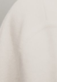 Cream-colored fabric with a soft, textured surface, featuring smooth lines and subtle folds. No visible hardware or patterns.