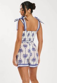Romper blanco con estampado de palmeras azules. Cuenta con tirantes a rayas en los hombros, un cuerpo fruncido y una cintura elástica con shorts. Textura suave.