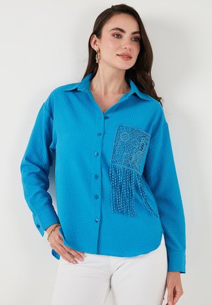 Blaues strukturiertes Hemd mit Knöpfen und einer Spitzen-Tasche mit Perlenbesatz. Lange Ärmel und ein Kragen runden das Design ab.