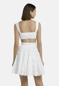Witte twee-delige outfit met een cropped top met brede schouderbanden en een rok met een gerimpelde zoom, beide gemaakt van textuurstof met gaatjesdetails.