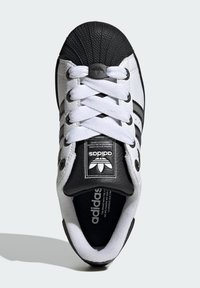 Biele kožené tenisky s čiernym gumeným špicom, s čiernymi pruhmi, plochými bielymi šnúrkami a označením na jazyku.