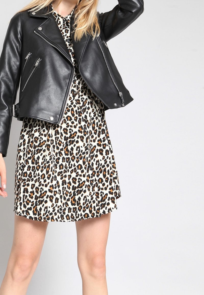 Musta nahkainen biker-takki kermaisen leopardi-kuvioisen mekon päällä. Takissa on vetoketjut ja hopeiset yksityiskohdat; mekko on A-linjainen.