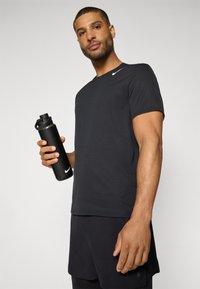 T-shirt de sport noir avec une surface texturée et des manches courtes, accompagné d'une bouteille d'eau noire avec un couvercle, le tout d'un style visuel minimaliste.