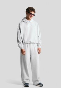 Felpa grigia chiara e pantaloni abbinati in materiale morbido, con cappuccio, polsini a coste e un piccolo logo sul petto.