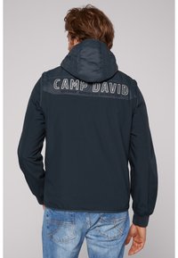 Jachetă cu glugă marină, cu o textură netedă, având brodat pe spate "CAMP DAVID", completată cu manșete și tiv cu nervuri.