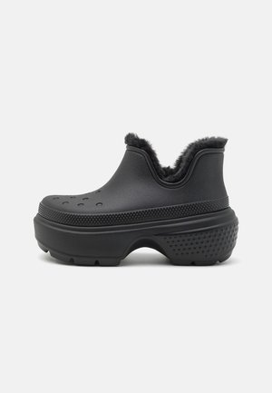 Zueco negro con plataforma, suela texturizada, orificios de ventilación en la parte superior y forro de piel negra y suave alrededor del tobillo.