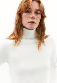 Witte coltrui gemaakt van een zacht gebreid materiaal, met een geribbelde halslijn en naadloos schouderontwerp. Gladde textuur met minimale details.