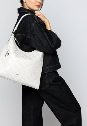 Weiße, gesteppte Lederhandtasche mit einer lässigen Silhouette, ausgestattet mit einem Metalldetail und einem verstellbaren Riemen, getragen zu einem dunkelblauen Denim-Outfit.