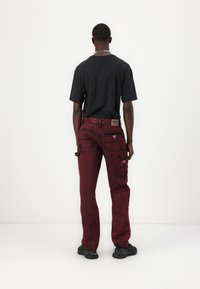 Røde denim cargo-bukser med flere lommer, sorte stikninger og en tekstureret finish. Kombineret med en simpel sort t-shirt og sorte sko.