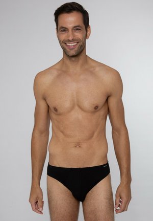Culotte noire en tissu côtelé, présentant un design ajusté avec une ceinture et sans marque visible. Le modèle se tient avec une expression neutre.