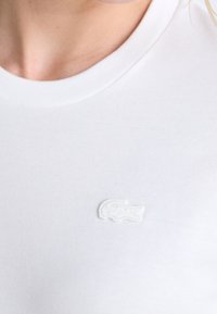White cotton t-shirt with a round neckline, featuring a small white embroidered crocodile logo on the left side of the chest.