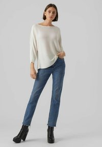 Weißer gerippter Strickpullover mit weitem Ausschnitt, kombiniert mit dunkelblauen hochtaillierten Jeans und schwarzen klobigen Ankle-Boots mit Absatz.