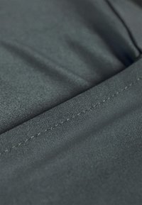 Tessuto grigio scuro con una superficie liscia e cuciture visibili. Il tessuto presenta un motivo sottile e si drappeggia leggermente. La finitura dei bordi è ordinata e pulita.