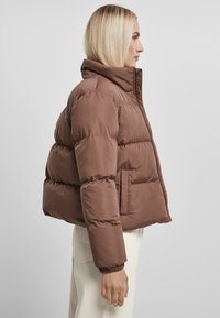 Brun pufferjakke med h�øj krave, der har et boxy design, contoureret syning og elastiske manchetter. Glat tekstur.