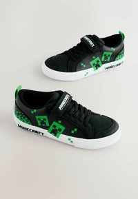 Zapatillas negras con patrones pixelados verdes, diseño con cordones, una correa de velcro y suelas de goma blancas. Marca "Minecraft" en el lateral.