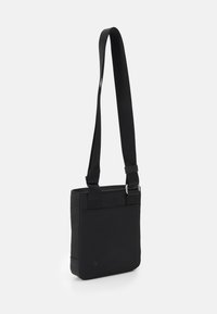 Borsa a tracolla nera realizzata in tessuto liscio, caratterizzata da una forma rettangolare, cinturino regolabile e design minimalista senza dettagli hardware visibili.