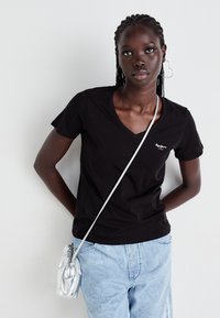 Černé bavlněné tričko s výstřihem do V a krátkými rukávy, doplněné o světle modré džíny a malou stříbrnou crossbody kabelku.