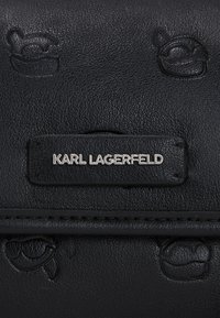 Borsa in pelle nera testurizzata con logo in rilievo e una targhetta metallica con il nome "KARL LAGERFELD". Finitura liscia con motivi sottili.