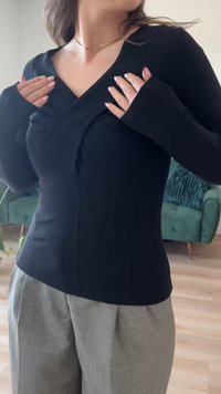 Svart langermet topp med V-hals og omslagdesign, laget av ribbet materiale. Har forlengede ermer med utsvingte mansjetter.
