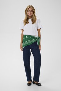 T-shirt bianco, avvolgente verde a strisce attorno ai fianchi, jeans blu a gamba dritta e scarpe basse nere. Texture morbide con motivi semplici.