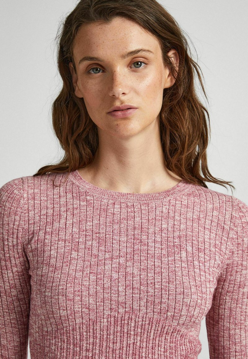 Maglione a coste di un rosa chiaro con scollatura rotonda, tessuto testurizzato e design aderente, caratterizzato da linee orizzontali e verticali.