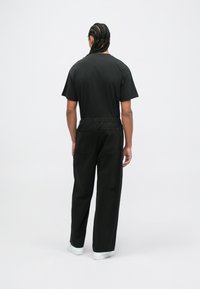 Svart kortermet t-skjorte kombinert med svarte avslappede bukser. Buksene har elastisk midje og romslige baklommer. Hvite joggesko.