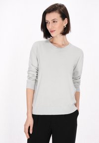 Hellgrauer Strickpullover mit rundem Ausschnitt, langen Ärmeln und gerippten Bündchen. Glatte Textur, kombiniert mit schwarzen Hosen. Einfaches Design.