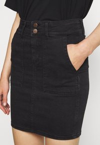 Zwarte denim rok met een aansluitend ontwerp, twee voorzakken, twee metalen knopen bij de taille en een nette zoom.