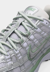 Λευκό και ανοιχτό πράσινο παπούτσι Nike με επάνω μέρος από δίχτυ, λεπτομερείς κορδόνια και κεντημένο λογότυπο Nike swoosh στο πλάι και στη γλώσσα.
