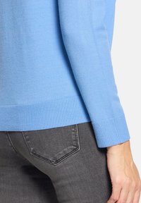 Pull bleu clair en maille avec poignets et ourlet côtelés, associé à un jean denim gris foncé. Accent mis sur la texture et le contraste des couleurs.