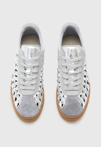 Sneakers argentati che presentano un mix di materiali lucidi e scamosciati, un design intrecciato testurizzato e una suola in gomma marrone. I lacci sono di un grigio chiaro.