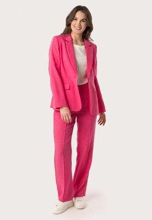 Pink blazer and matching pants in a fitted design, made from a textured fabric, paired with a white top and white sneakers.