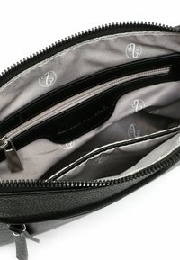 Interior de un bolso de cuero negro con un forro gris que presenta un sutil patrón de logotipos, bolsillo con cremallera y compartimentos organizadores.