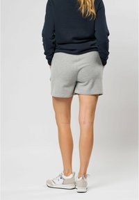 Šedé bavlněné šortky s volnějším střihem a hladkou texturou. Nošeny s tmavě modrým tričkem s dlouhým rukávem a světlejšími teniskami.