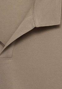 Tejido de camisa polo marrón con un tejido texturizado, que presenta un collar puntiagudo y costuras cuidadas a lo largo de los bordes.